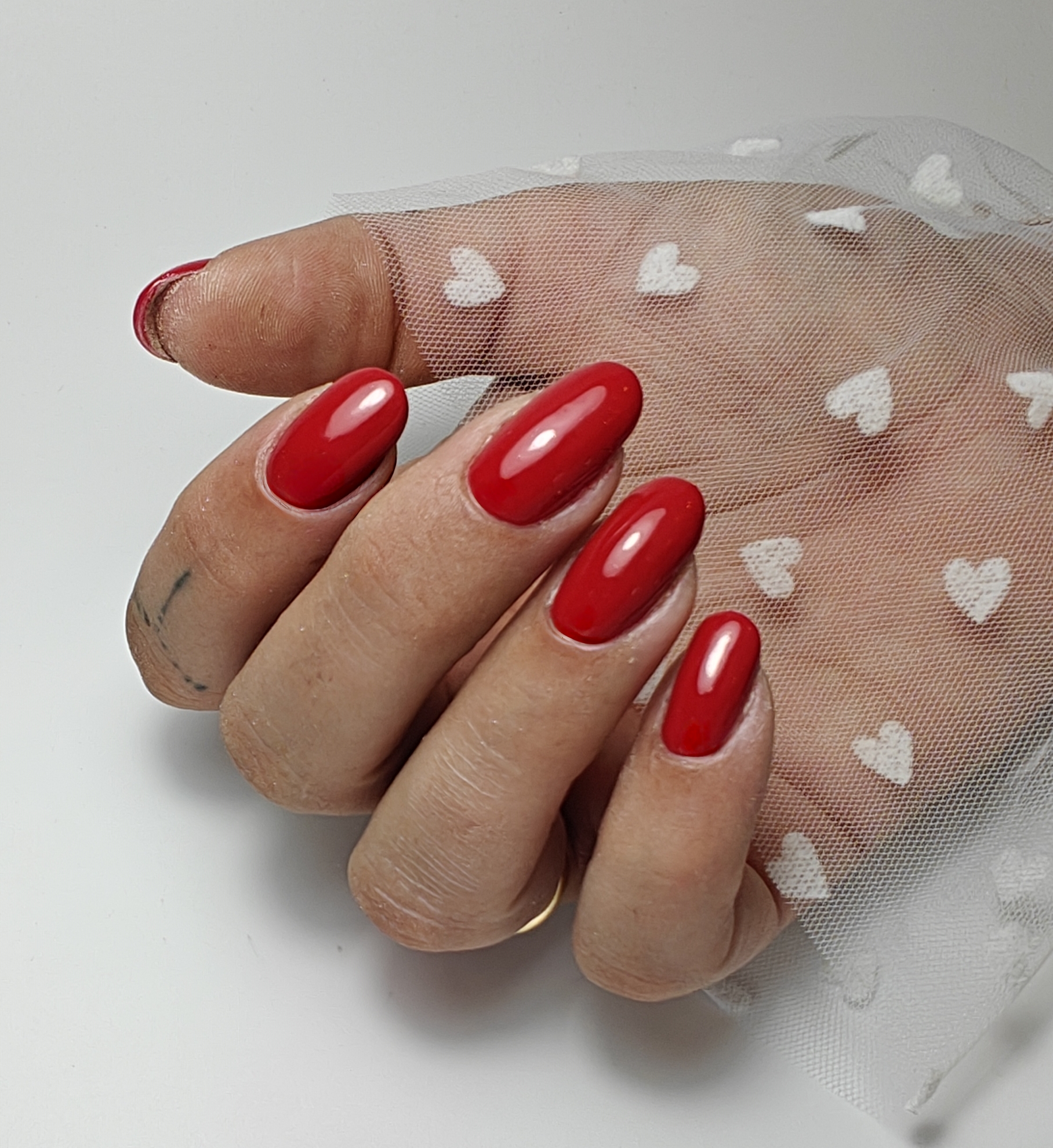 Rode amandelvormige nagels, de hand rust op tule met witte hartjes