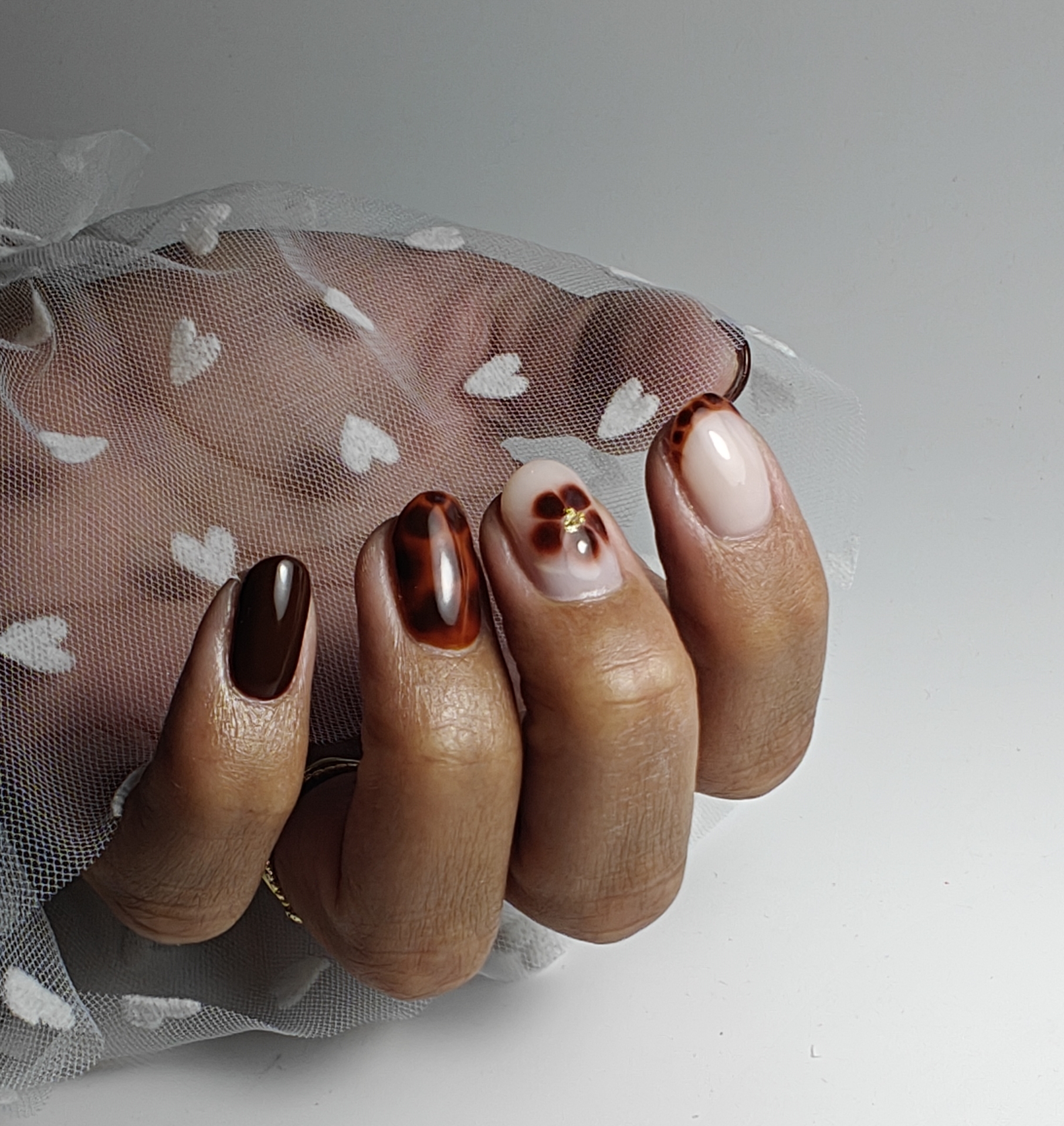 Bruine nagels met tortoise-design, de hand achter tule met hartjes