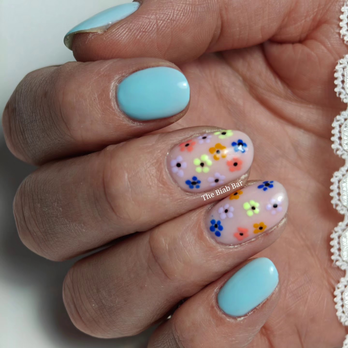 Lichtblauwe nagels met twee nagels vol gekleurde bloemetjes